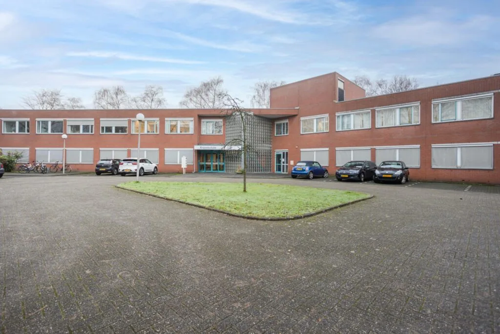 Vooraanzicht van het rode bakstenen gebouw aan de Christiaan Krammlaan met parkeervakken en fietsenrekken.